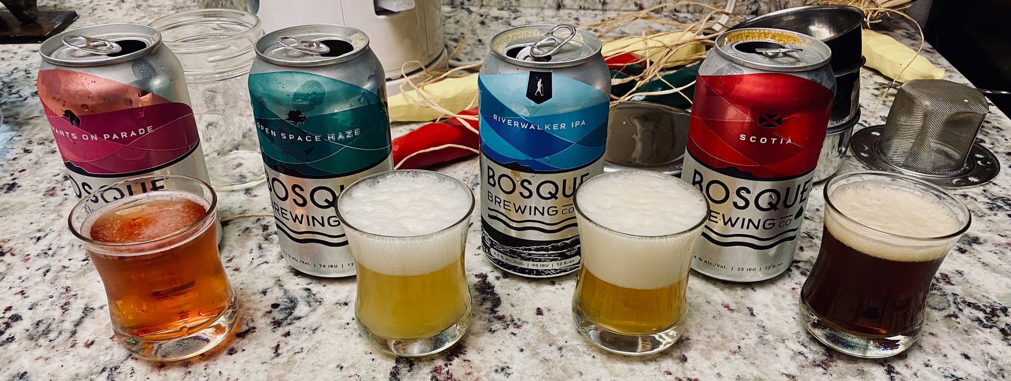 Four beer cans and poured beers from Bosque Brewing Co.