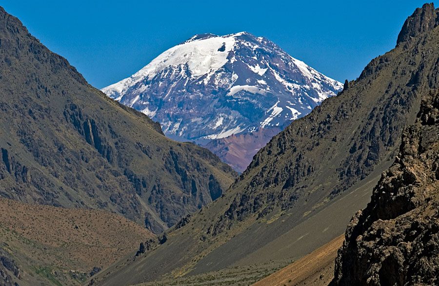 Snow-capped Mount Tupungato seen between two brown-green slopes