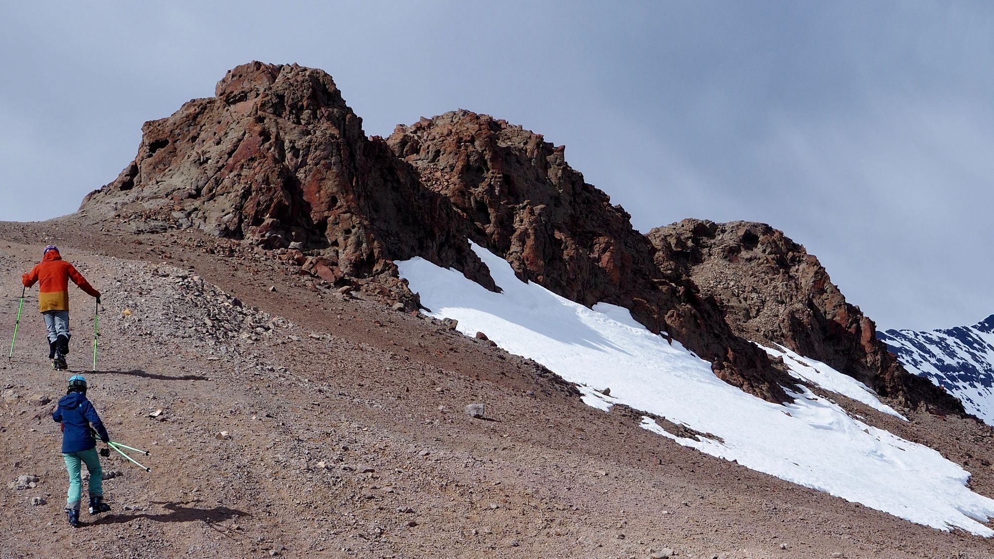 Photo of three large rocks on top of a ridge; two skiers hike up to them.