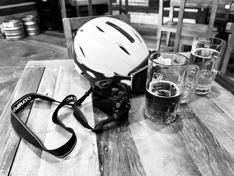 A ski helmet, Olympus camera, and two steins of beer on a wooden table.