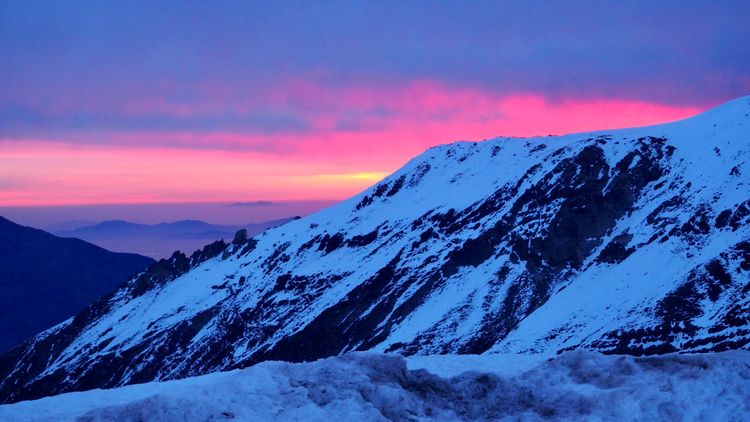 Sunset: stripes of pink surround bands of gold and orange behind a snow-covered mountain.